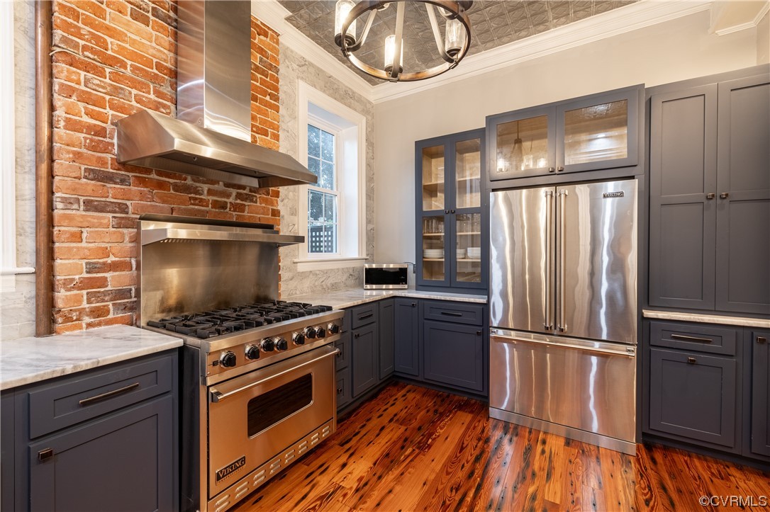 Kitchen with wall chimney range hood, high quality appliances, dark wood-type flooring, ornamental molding, and tasteful backsplash