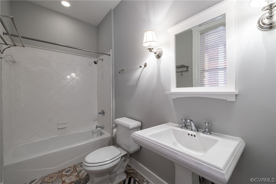 Full bathroom with tiled shower / bath, toilet, tile floors, and sink