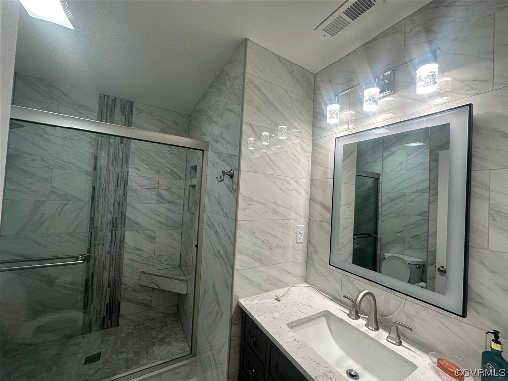 Bathroom with vanity, a shower with door, tile walls, and toilet