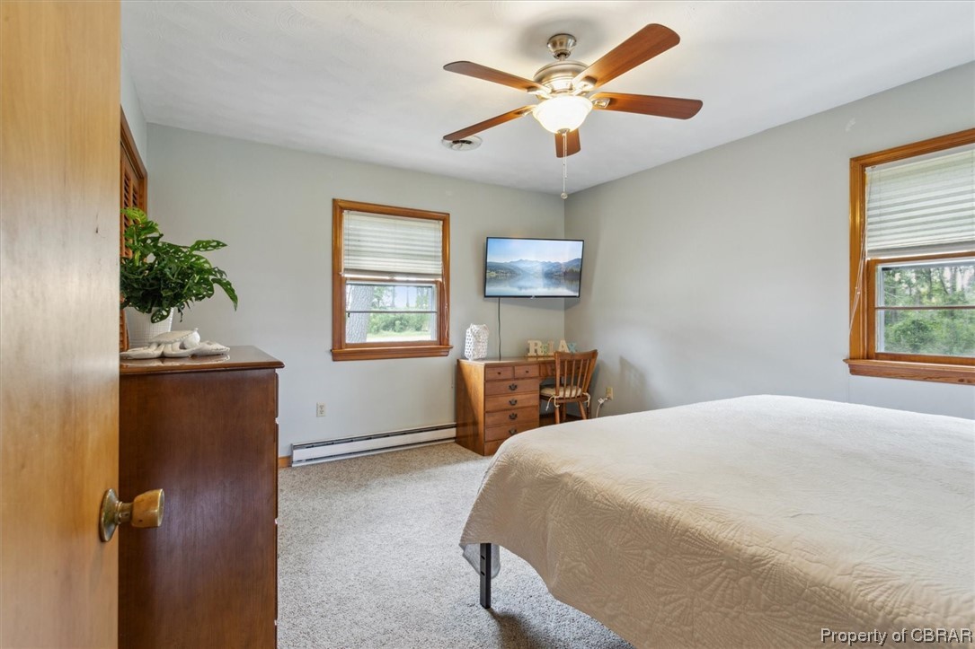 Bedroom featuring multiple windows, a baseboard heating unit, ceiling fan, and light colored carpet