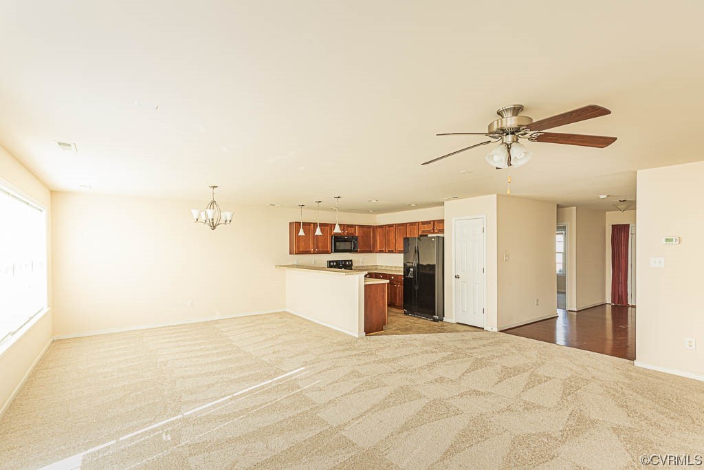 Unfurnished living room with light colored carpet and ceiling fan with notable chandelier