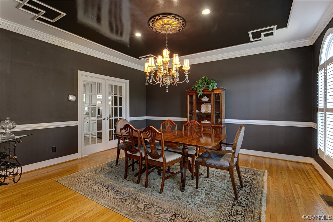 Dining area with french doors, designer chandelier, light wood flooring, and ornamental molding