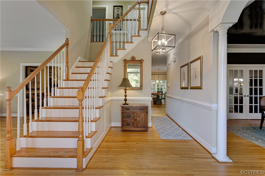 Stairway featuring a notable chandelier, columns, crown molding, and light hardwood  floors
