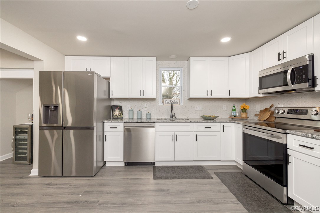 Kitchen with sink, appliances with stainless steel finishes, wine cooler, white cabinets, and light wood-type flooring