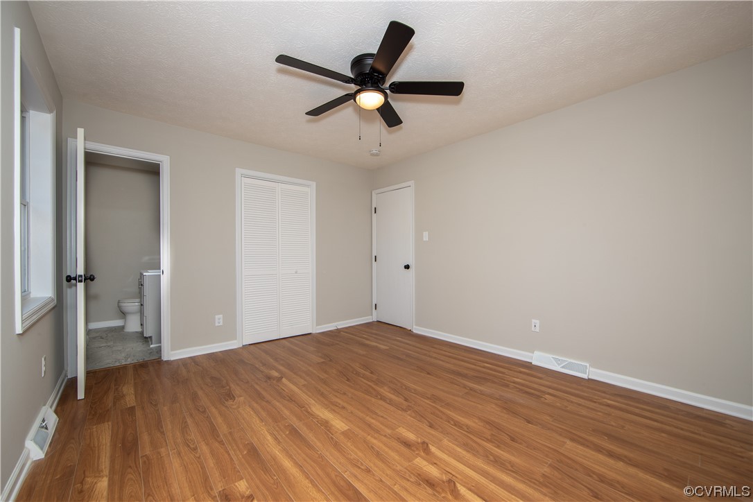 Unfurnished bedroom with ceiling fan, a textured ceiling, a closet, light hardwood / wood-style flooring, and connected bathroom