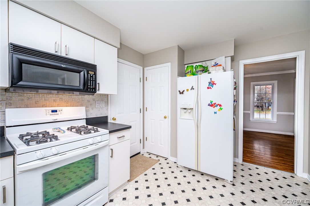 Kitchen with white appliances, ornamental molding, backsplash, light tile floors, and white cabinetry