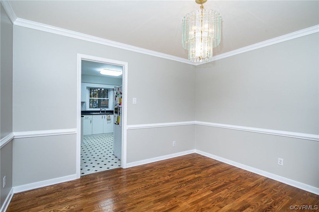 Unfurnished room with dark hardwood / wood-style flooring, an inviting chandelier, and ornamental molding