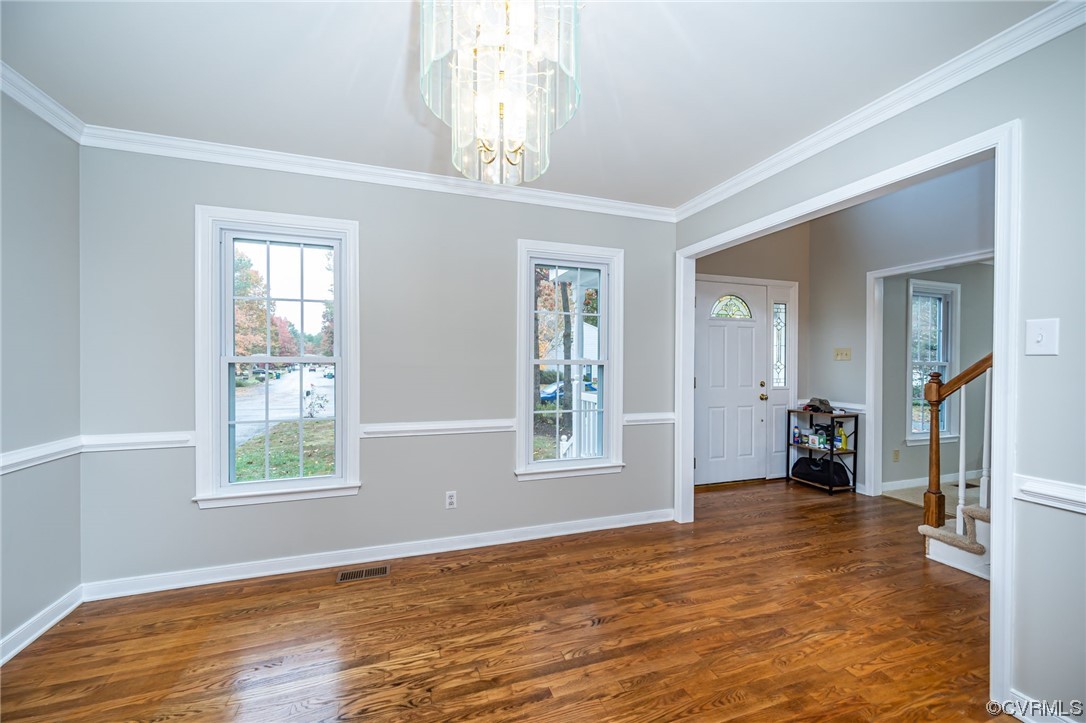 Spare room with an inviting chandelier, dark wood-type flooring, and crown molding