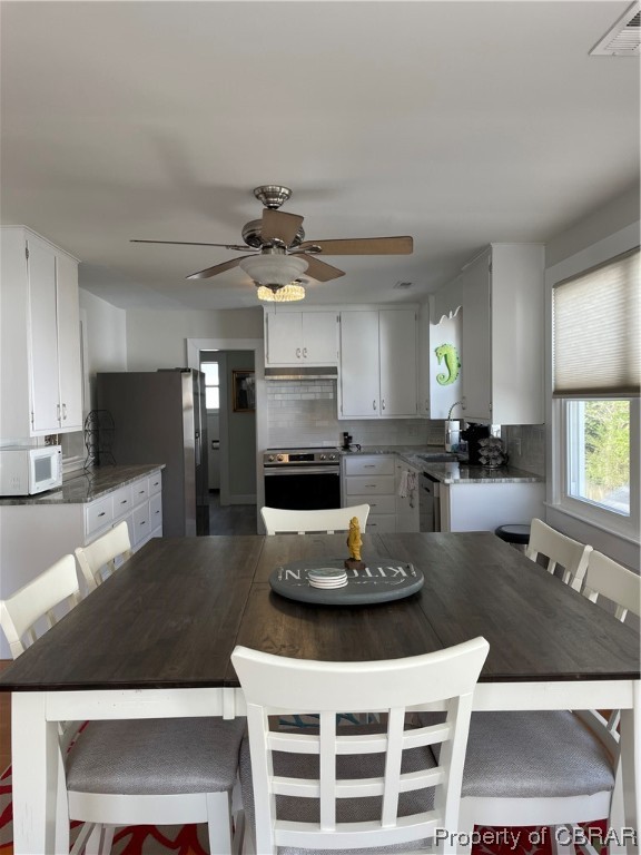 Kitchen featuring stove, ceiling fan, fridge, white cabinets, and tasteful backsplash