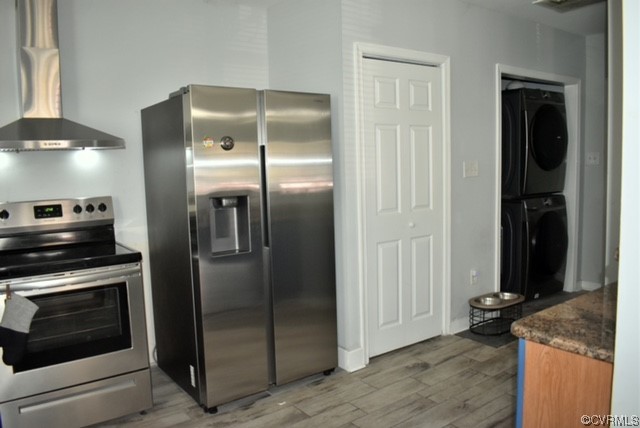 Kitchen featuring appliances, chimney range hood, dark countertops, & light wood-type flooring