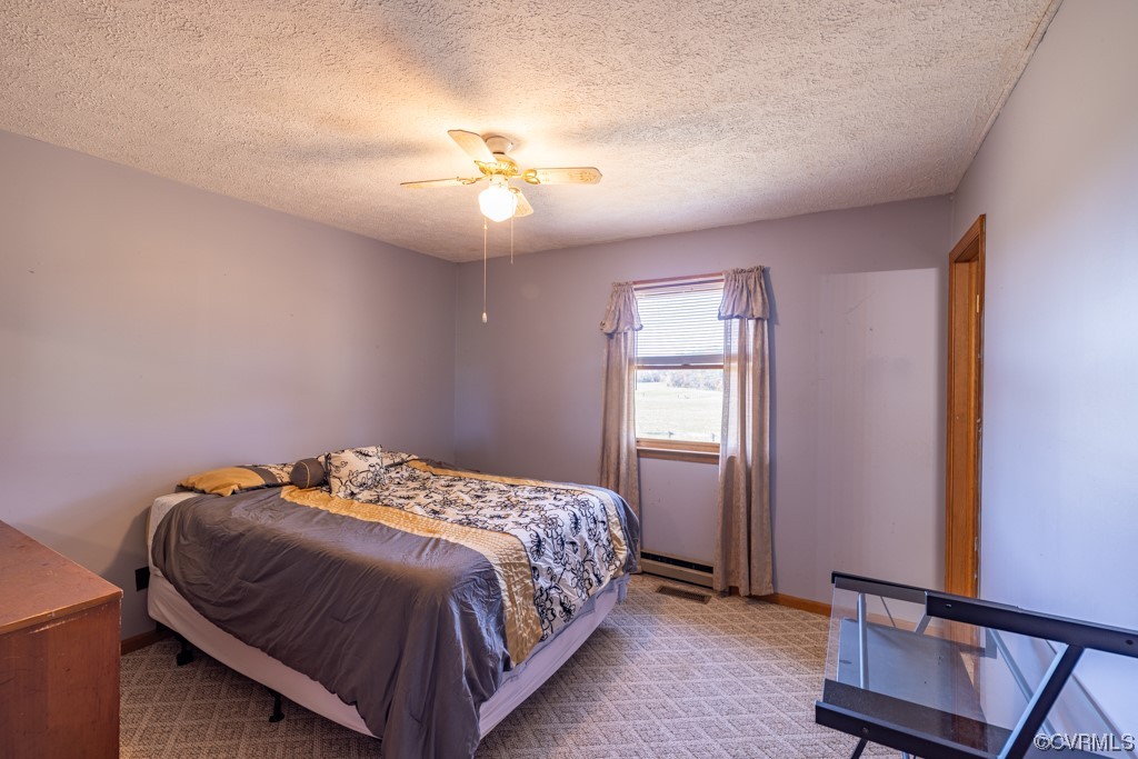 Carpeted bedroom featuring ceiling fan, a textured ceiling, and baseboard heating