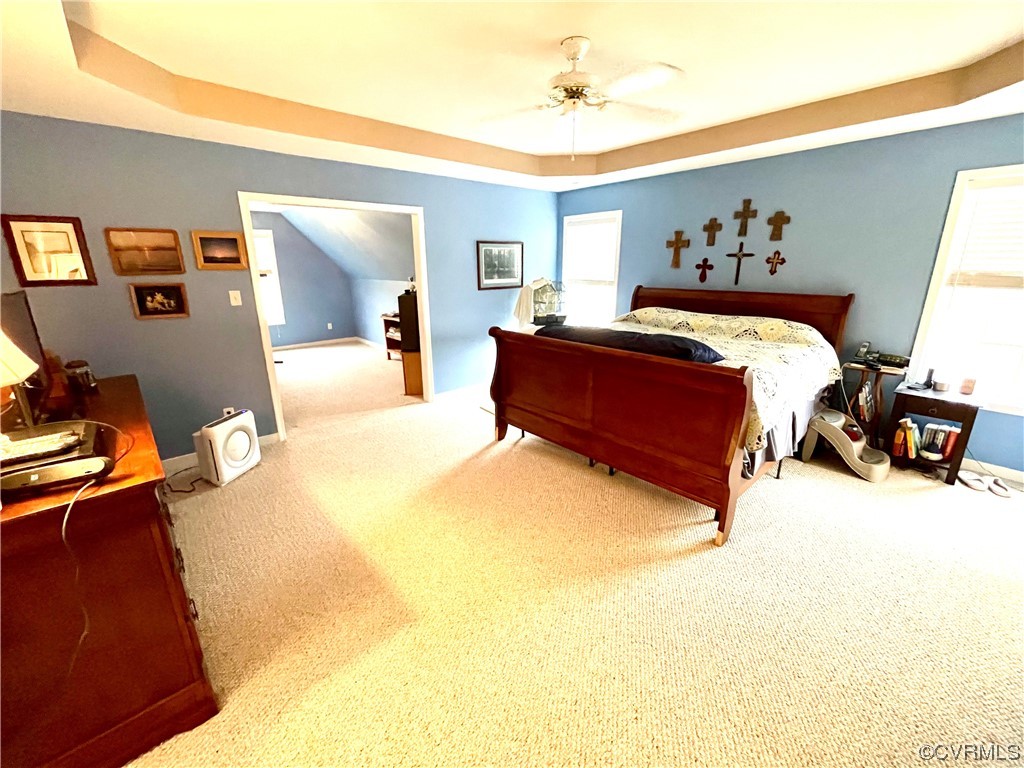 Carpeted bedroom with a raised ceiling and ceiling fan