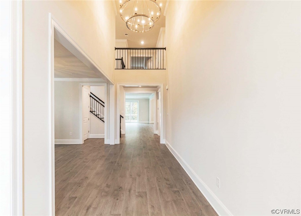Hall featuring an inviting chandelier, a towering ceiling, crown molding, and light hardwood / wood-style floors
