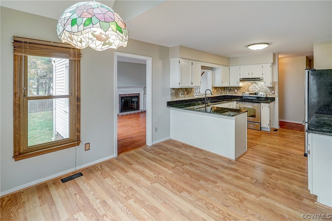 Kitchen with stainless steel range with electric stovetop, backsplash, light hardwood / wood-style flooring, a brick fireplace, and kitchen peninsula