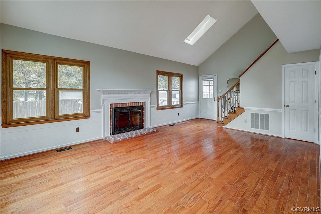 Family room featuring a skylight, a fireplace, high vaulted ceiling, and light hardwood / wood-style floors