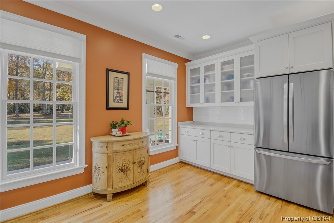 Kitchen offers a healthy amount of sunlight, stainless steel fridge, polished hardwood floors, and white cabinetry