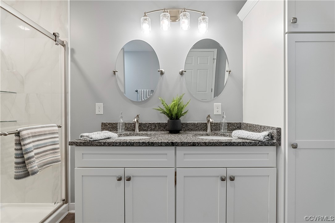 Bathroom featuring dual sinks, a shower with shower door, and large vanity