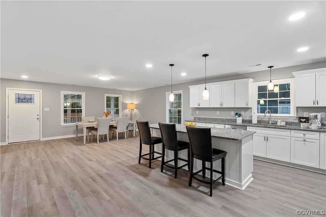 Kitchen with decorative light fixtures, white cabinets, sink, and light hardwood / wood-style flooring