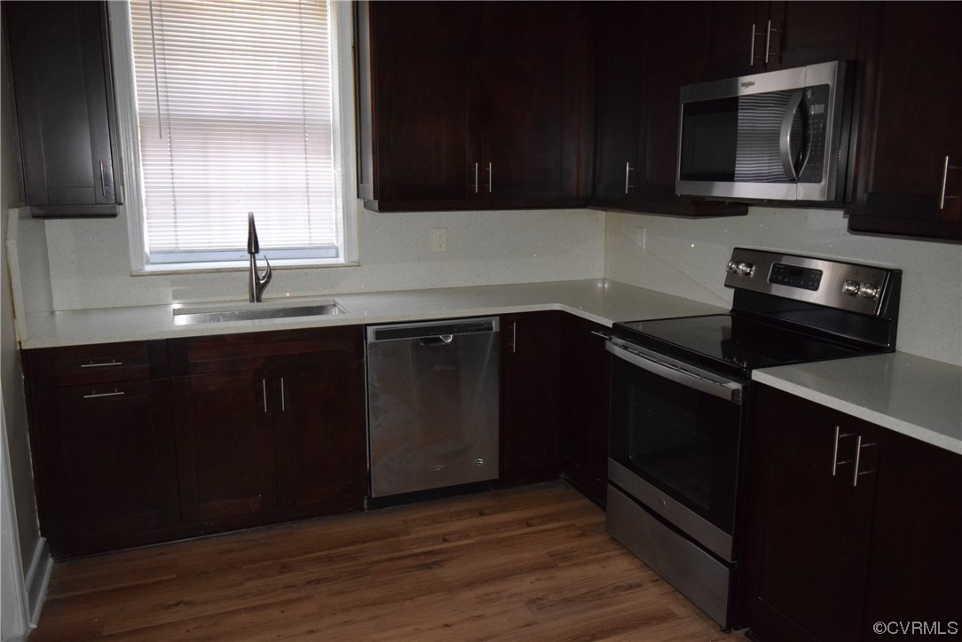 Kitchen with dark hardwood / wood-style flooring, sink, dark brown cabinetry, and stainless steel appliances