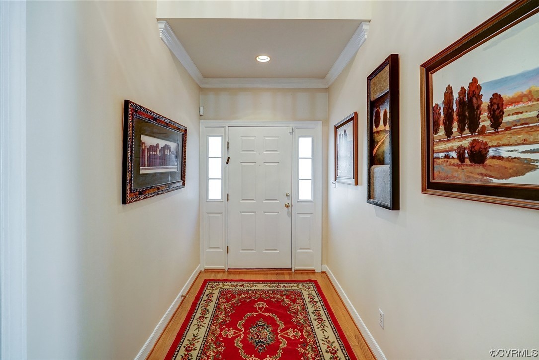 Foyer featuring crown molding and light hardwood floors opening into atrium