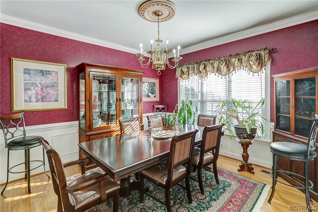 Bright dining room featuring hardwood flooring, crown molding, and a chandelier