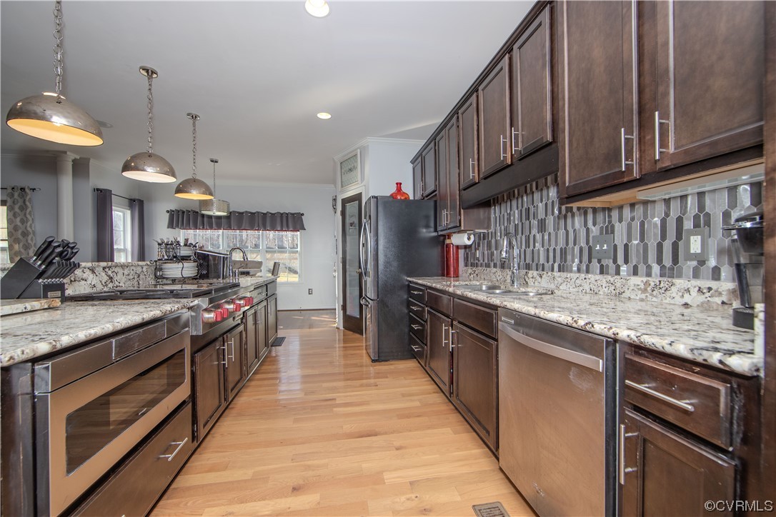 Kitchen featuring appliances with stainless steel finishes, light wood-type flooring, decorative light fixtures, and backsplash