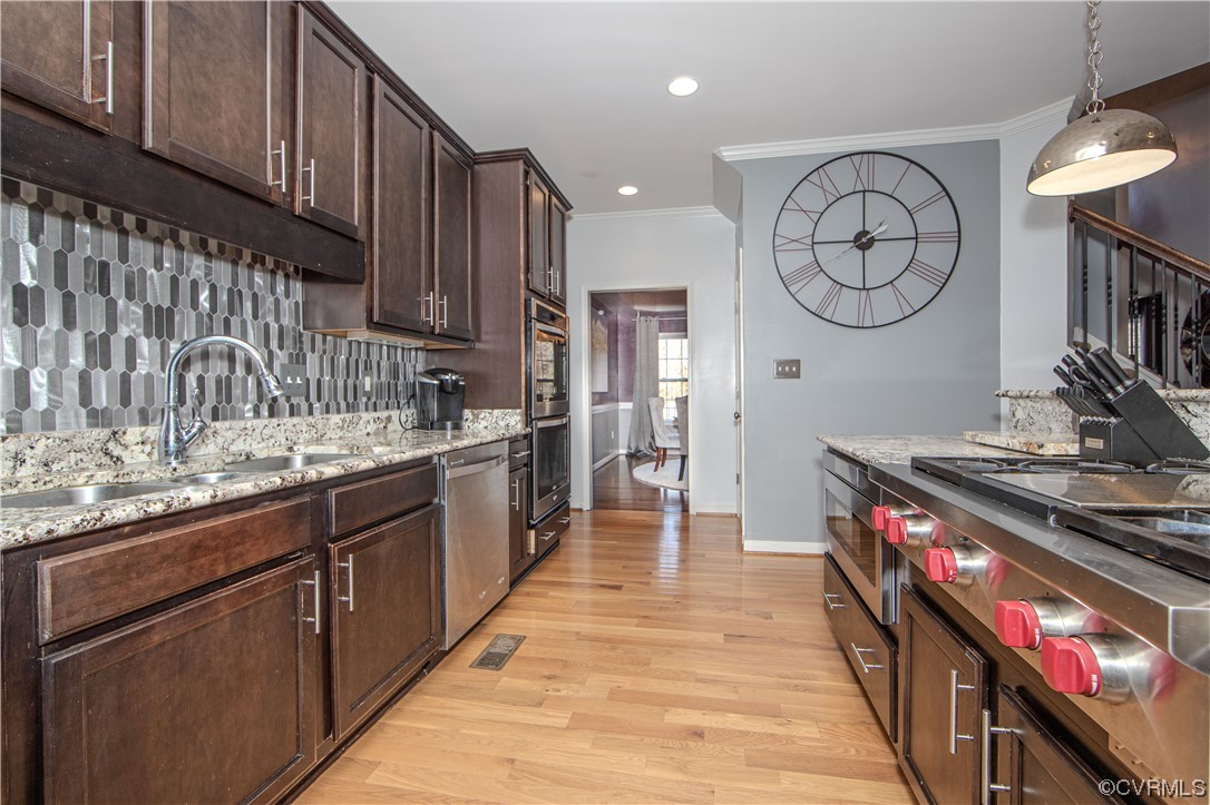 Kitchen featuring appliances with stainless steel finishes, light hardwood / wood-style floors, light stone countertops, decorative light fixtures, and backsplash
