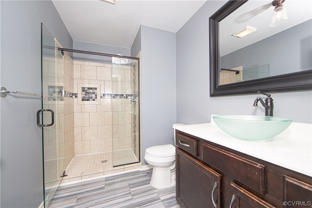 Bathroom with toilet, tile flooring, a shower with door, and vanity with extensive cabinet space