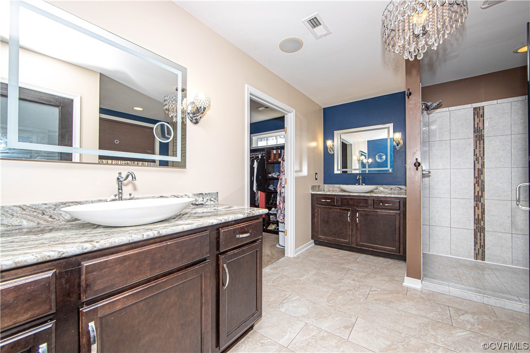 Bathroom featuring oversized vanity, a chandelier, a tile shower, tile flooring, and dual sinks