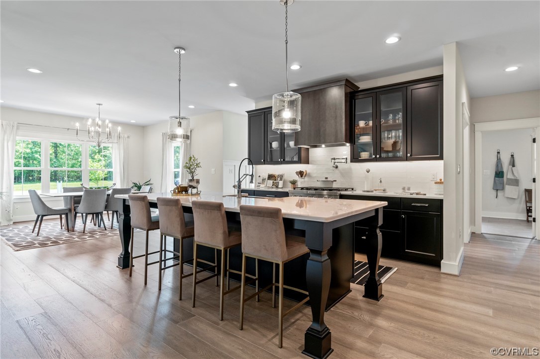 Kitchen featuring an island with sink, hanging light fixtures, tasteful backsplash, a notable chandelier, and light hardwood / wood-style flooring
