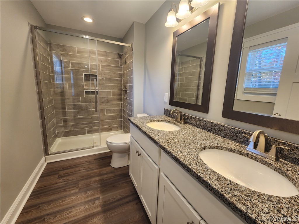 Bathroom featuring toilet, oversized vanity, dual sinks, hardwood / wood-style flooring, and a shower with shower door