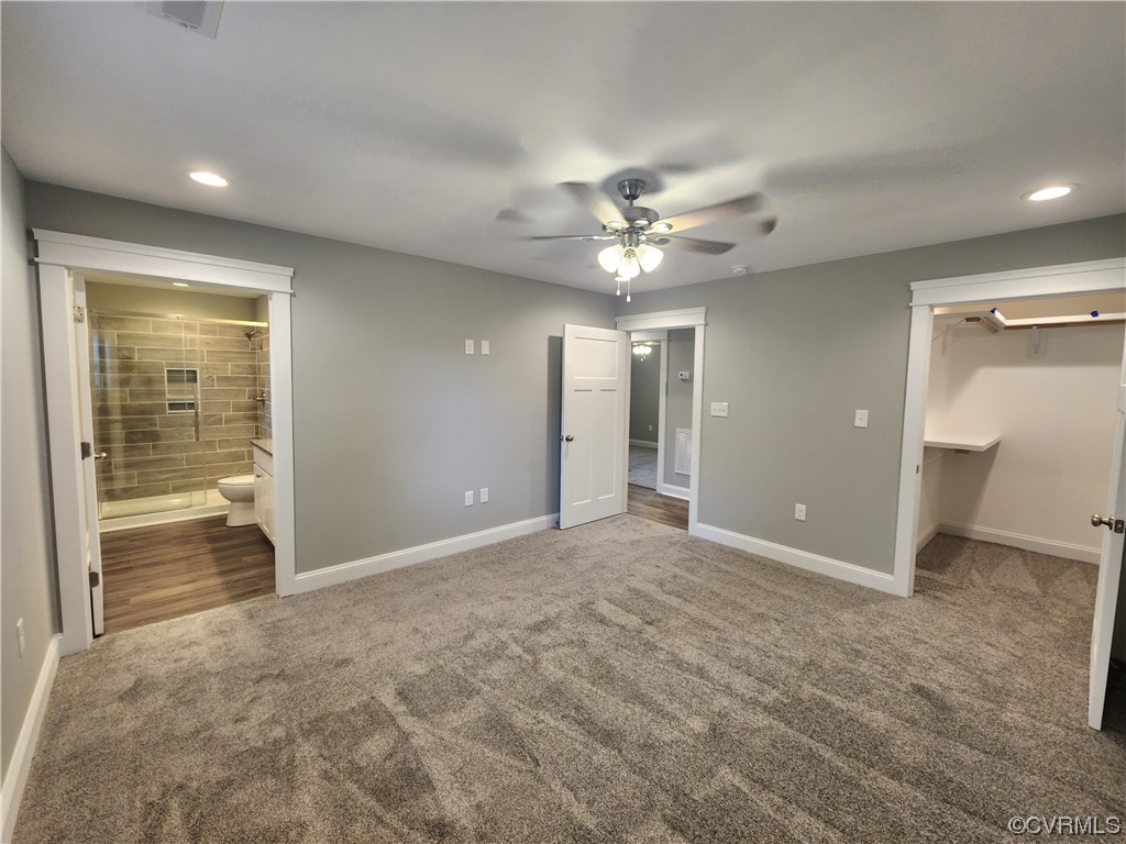 Unfurnished bedroom featuring a walk in closet, ensuite bath, ceiling fan, and carpet