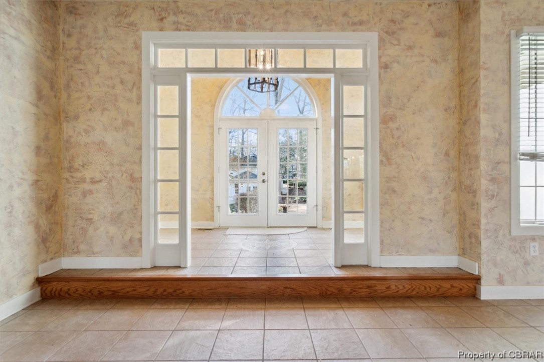 Foyer entrance with light tile flooring, a notable chandelier, a wealth of natural light, and french doors