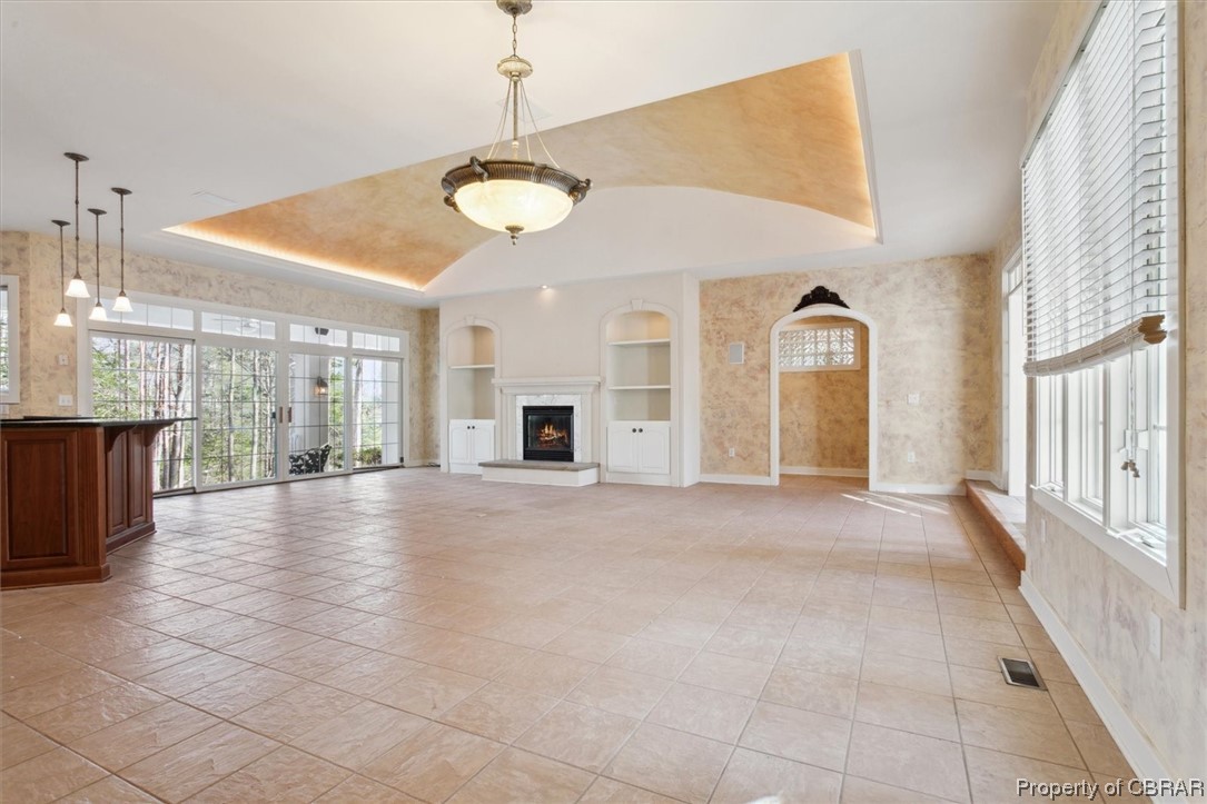 Unfurnished living room with light tile floors, a tray ceiling, and built in features