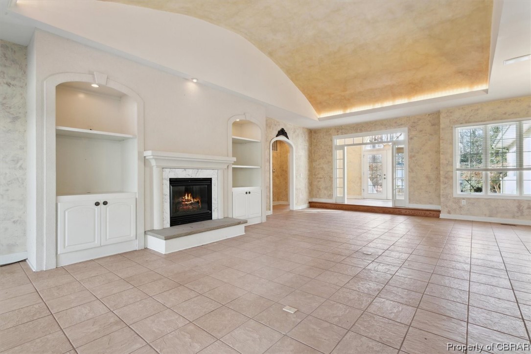 Unfurnished living room with a high end fireplace, a raised ceiling, built in shelves, and light tile floors