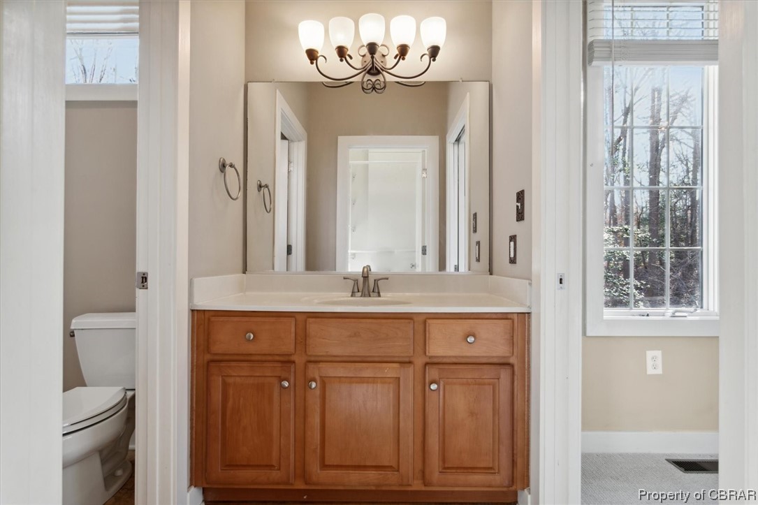 Bathroom featuring toilet, a notable chandelier, a healthy amount of sunlight, and vanity