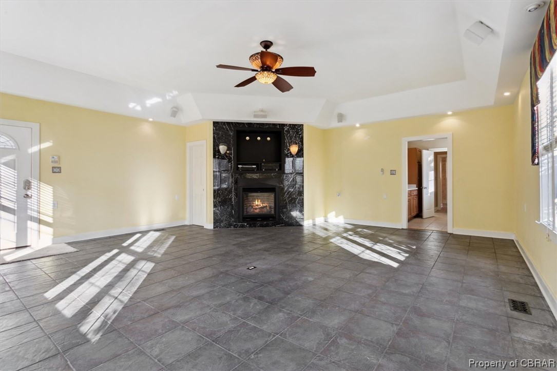 Unfurnished living room featuring dark tile flooring, a high end fireplace, a raised ceiling, and ceiling fan