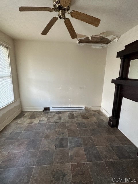 Empty room with dark tile floors, ceiling fan, and a baseboard radiator