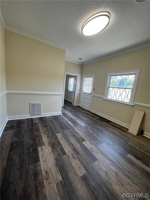 Empty room featuring dark wood-type flooring, ornamental molding, and a textured ceiling
