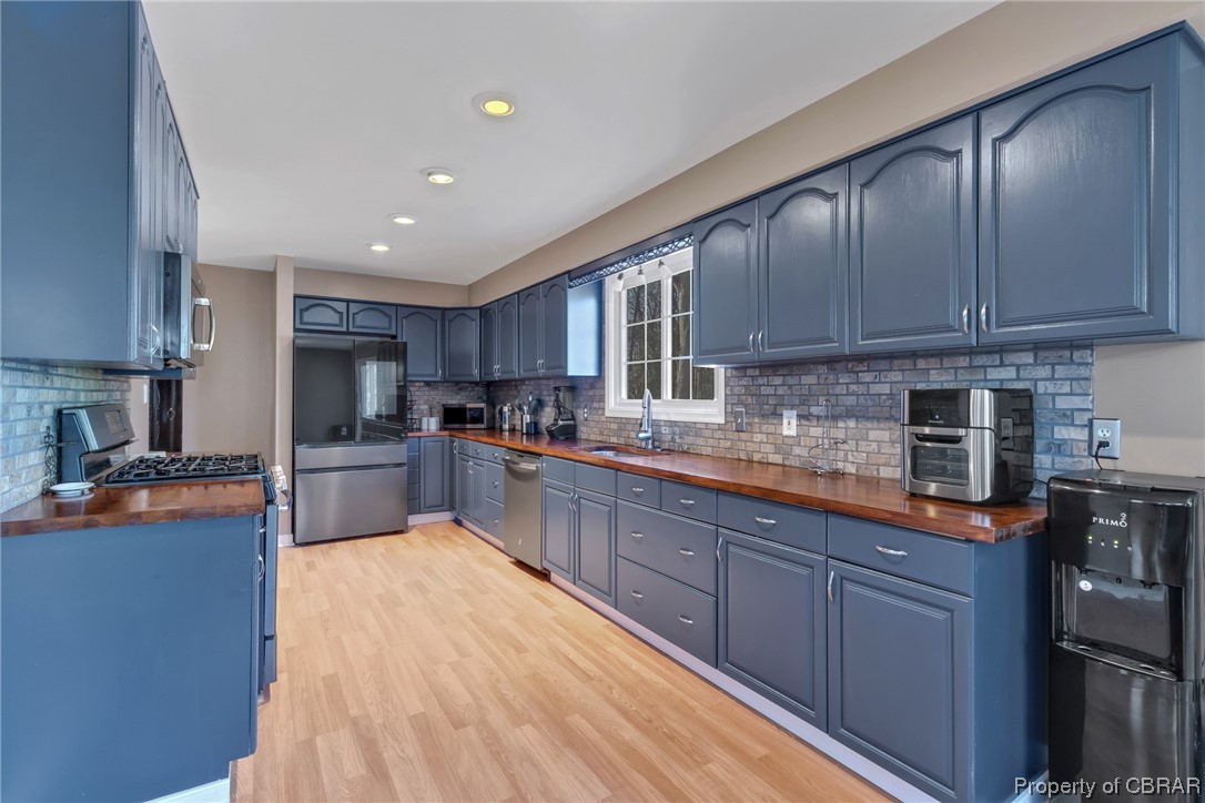 Kitchen featuring tasteful backsplash, light hardwood / wood-style flooring, blue cabinets, sink, and stainless steel appliances