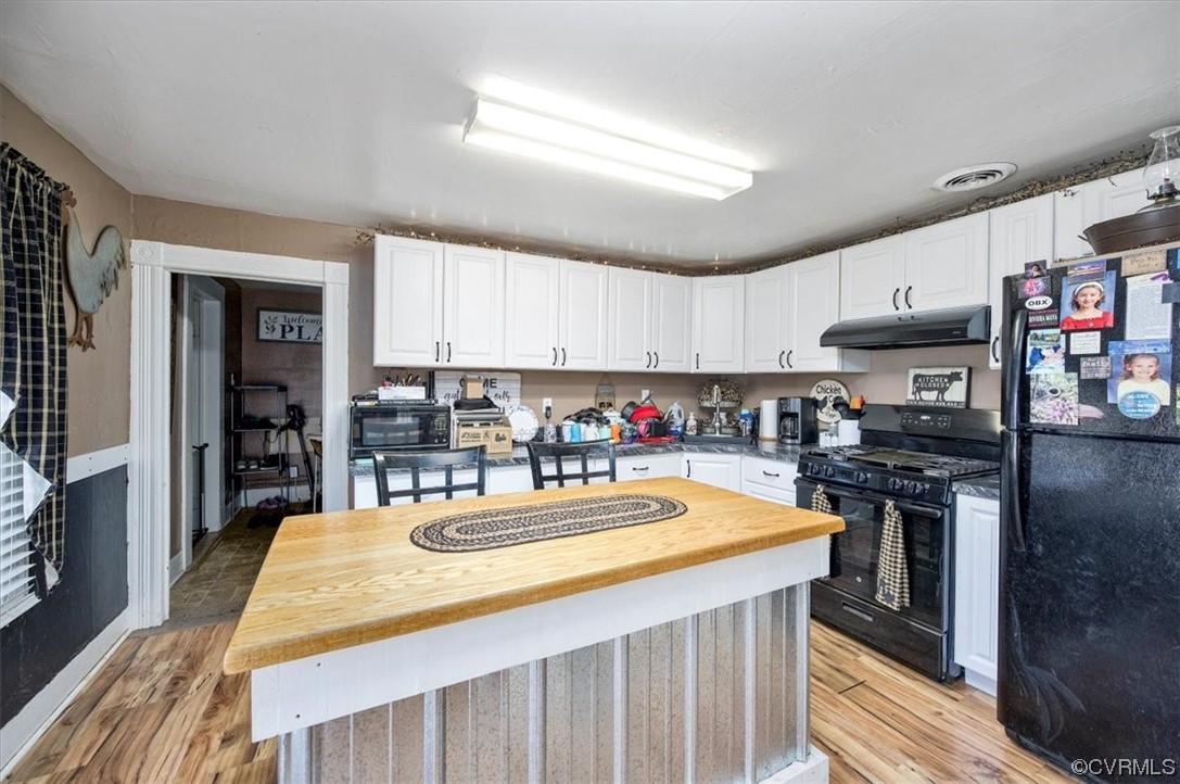Kitchen with black appliances, butcher block countertops, white cabinets, a center island, and light hardwood / wood-style flooring