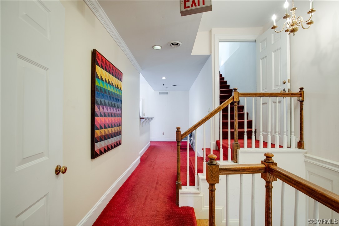 Stairs featuring a chandelier, crown molding, and dark carpet