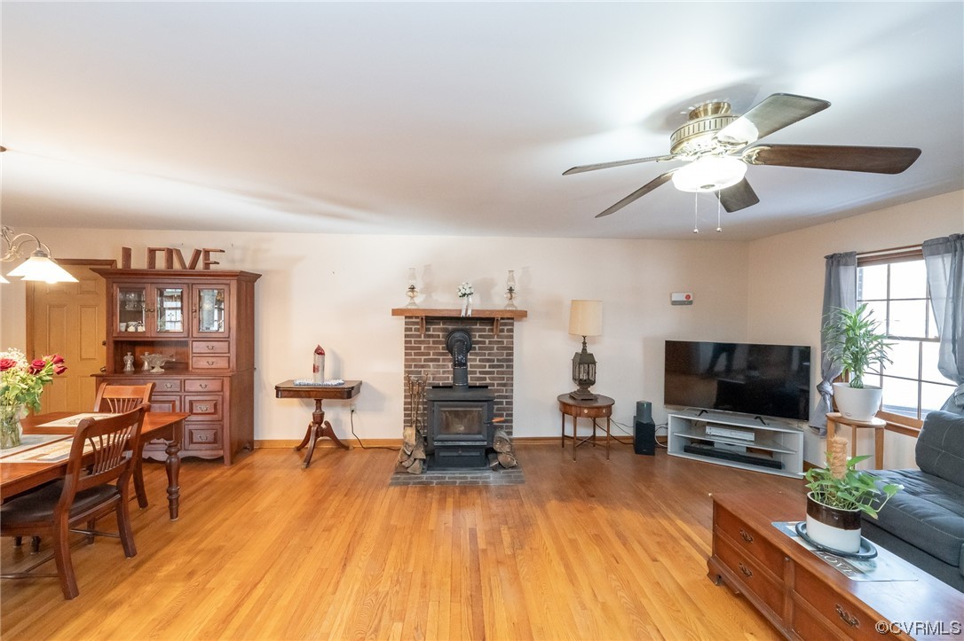 Living room with light hardwood / wood-style floors, a wood stove, and ceiling fan