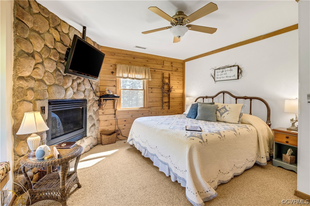 Carpeted bedroom with crown molding, wooden walls, a fireplace, and ceiling fan