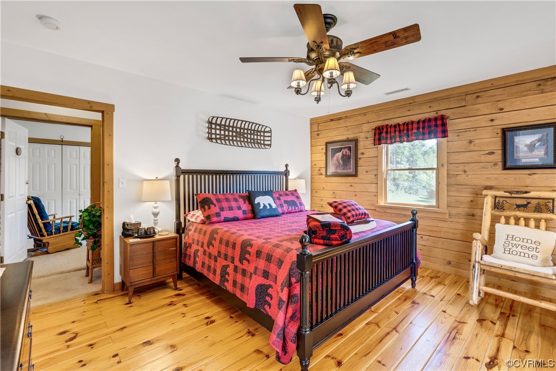 Bedroom featuring light wood-type flooring, wooden walls, and ceiling fan
