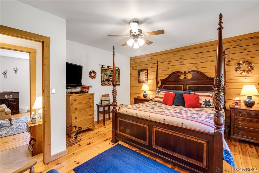 Bedroom with light hardwood / wood-style floors, wooden walls, and ceiling fan