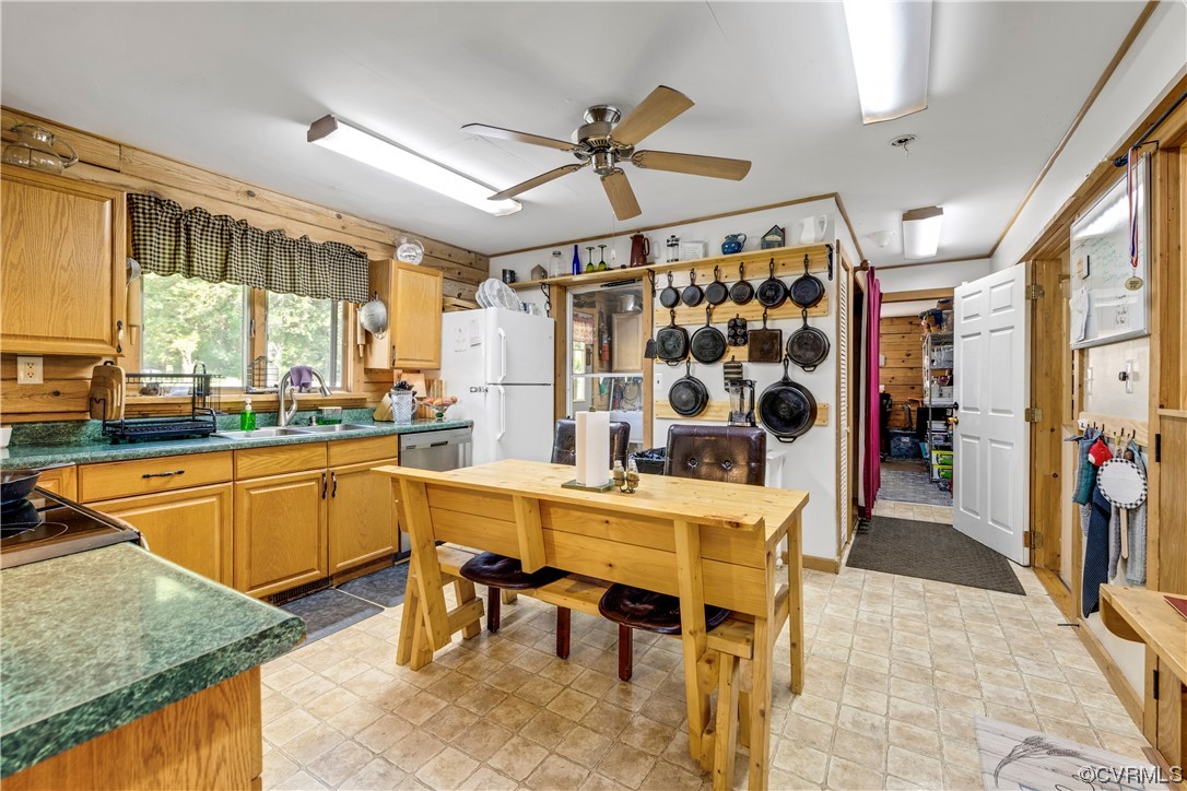 Kitchen featuring wood walls, ceiling fan, sink, white fridge, and light tile flooring