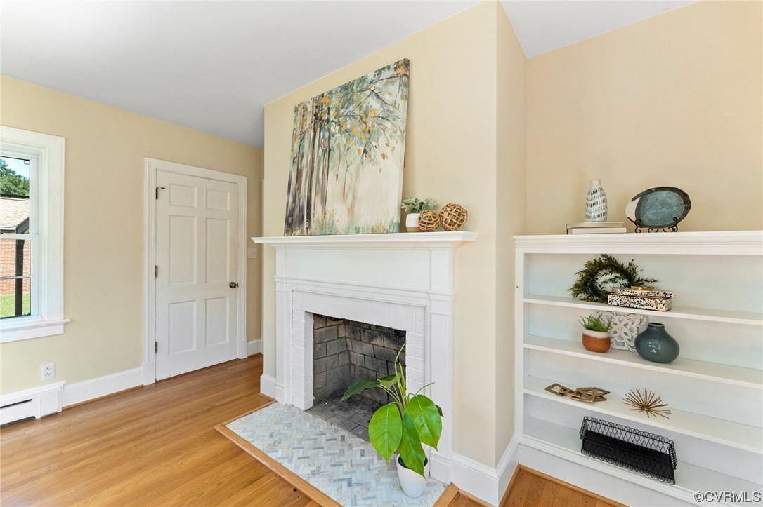 Living room with light hardwood / wood-style flooring, baseboard heating, and a brick fireplace