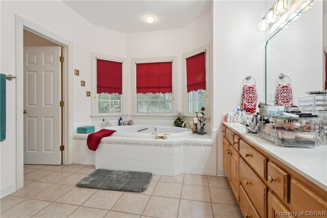 Bathroom featuring vanity, a relaxing tiled bath, and tile flooring
