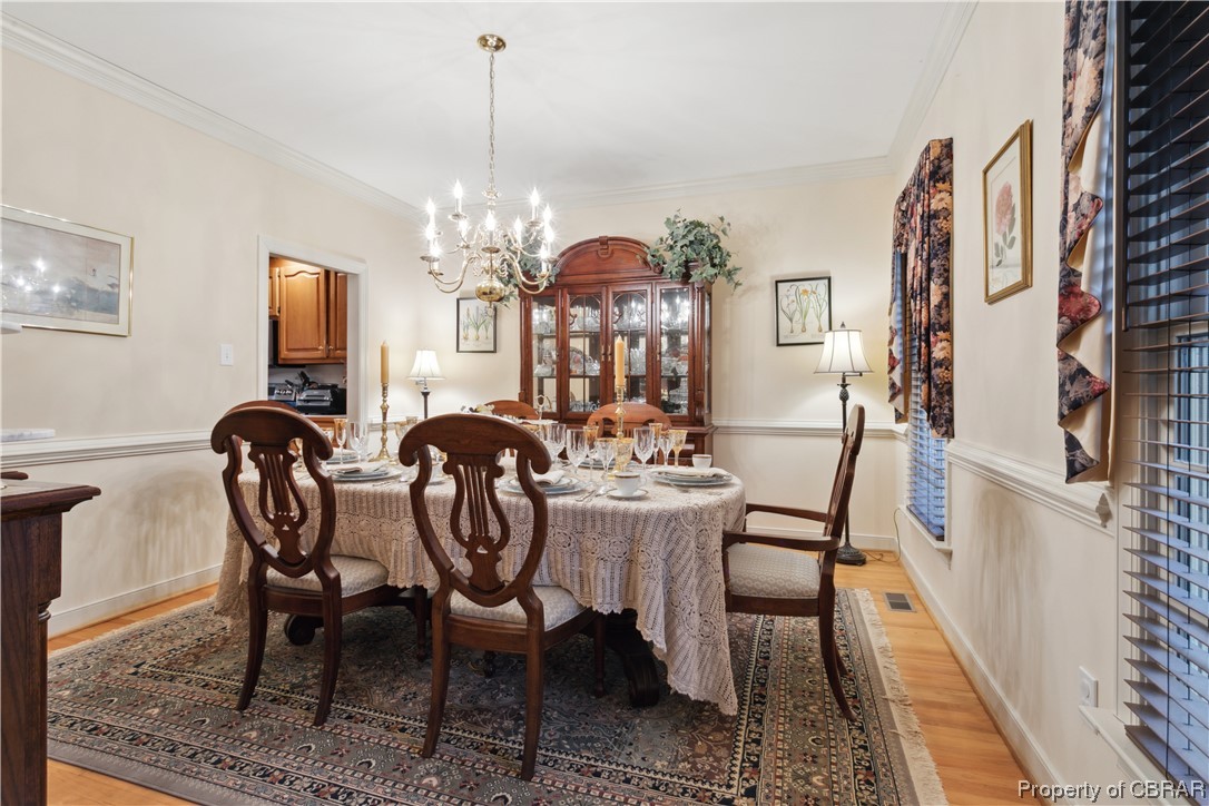 Dining room featuring light hardwood / wood-style floors, ornamental molding, and a notable chandelier